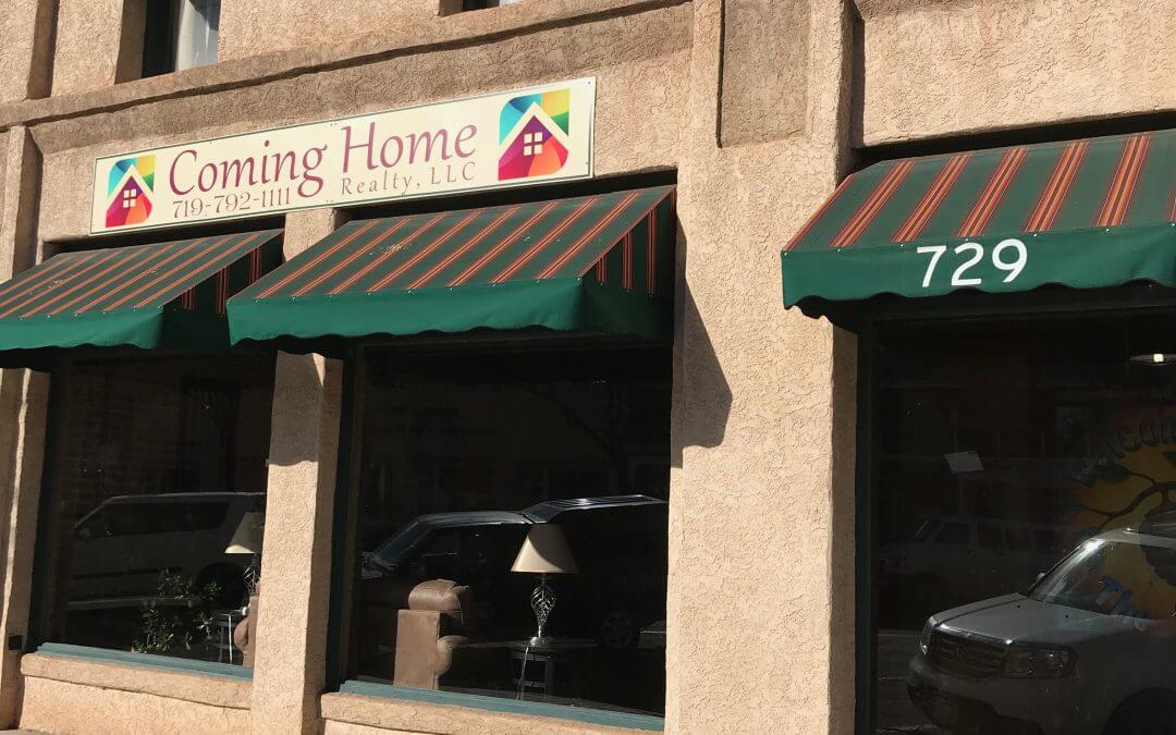 An exterior image of the Coming Home Realty windows with green and maroon striped awnings and signage